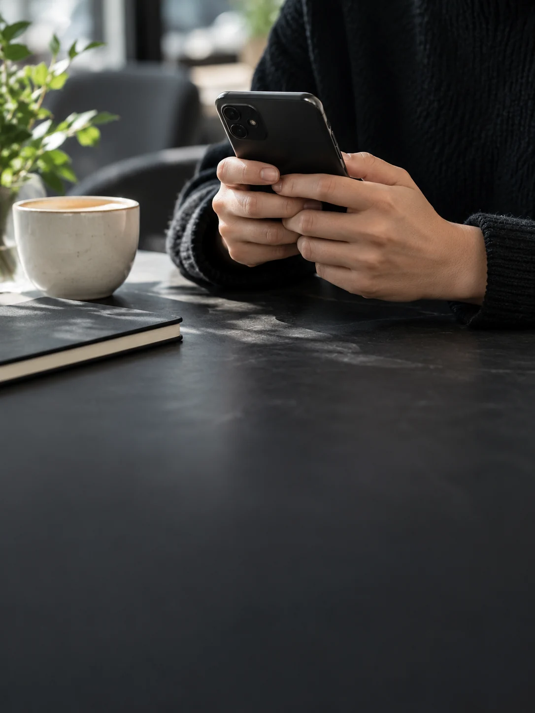 Symbolbild: Hände mit einem Smartphone an einem Tisch mit Kaffee und Notizbuch